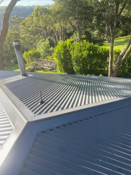 Grey metal hip roof with a flue pipe, above a garden