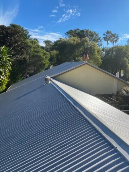 Light grey metal roof finished up to a gable end, with a roofer on the ridge
