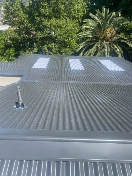 Grey metal roof with translucent skylight sheets and a vent pipe