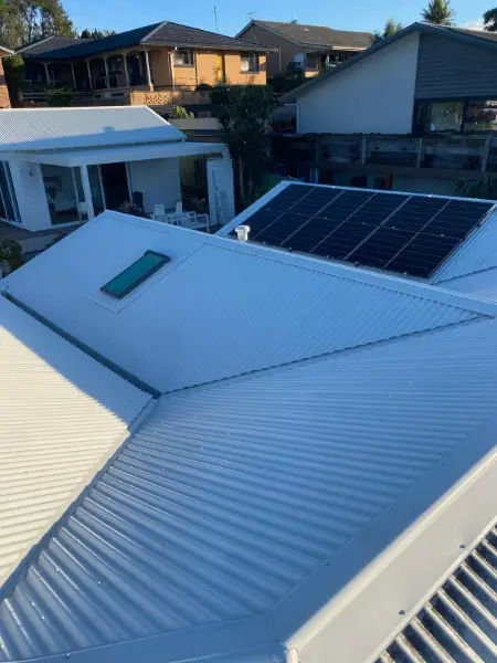 Pale metal roof with a skylight and solar panels on a hillside home