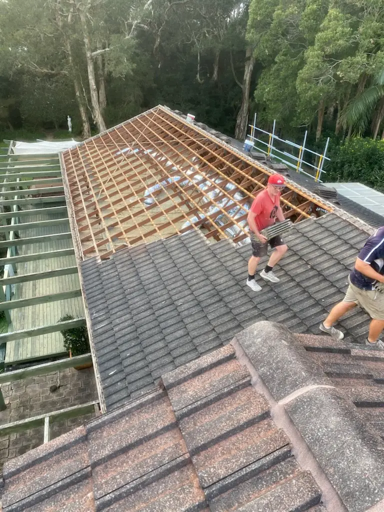 Roofers stripping old concrete tiles to expose the timber battens before a new metal roof goes on